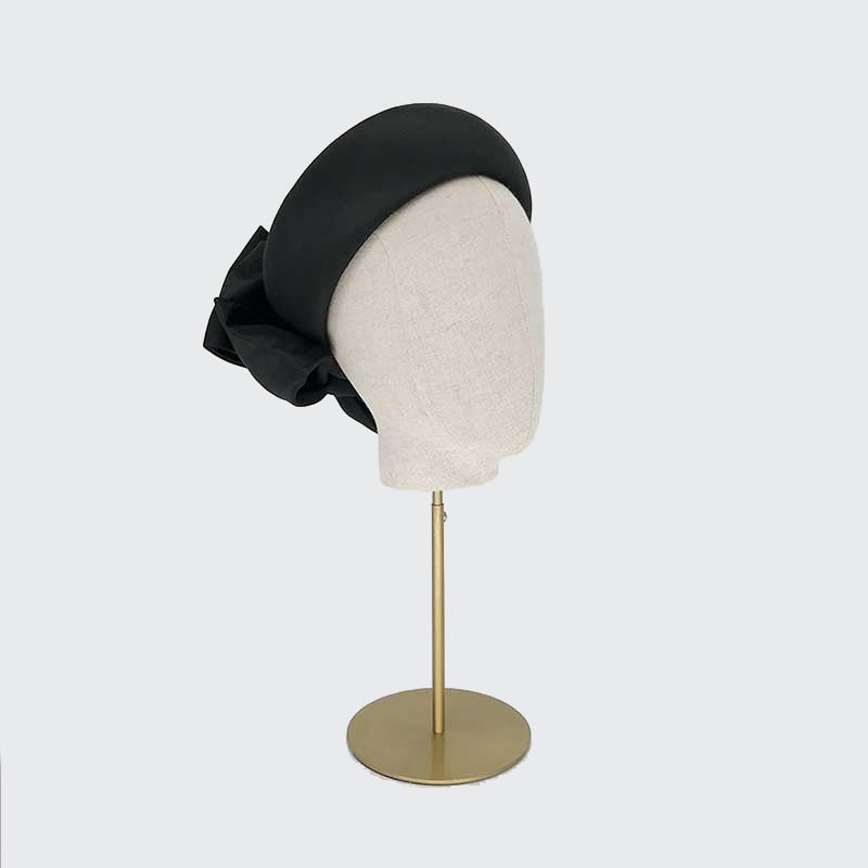 Side view of a black taffeta silk Jackie O pillbox with bows on a linen display head