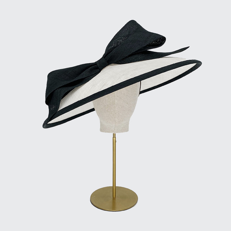 Photo of a white sweep bell with a black edge and a large bow on a linen display head