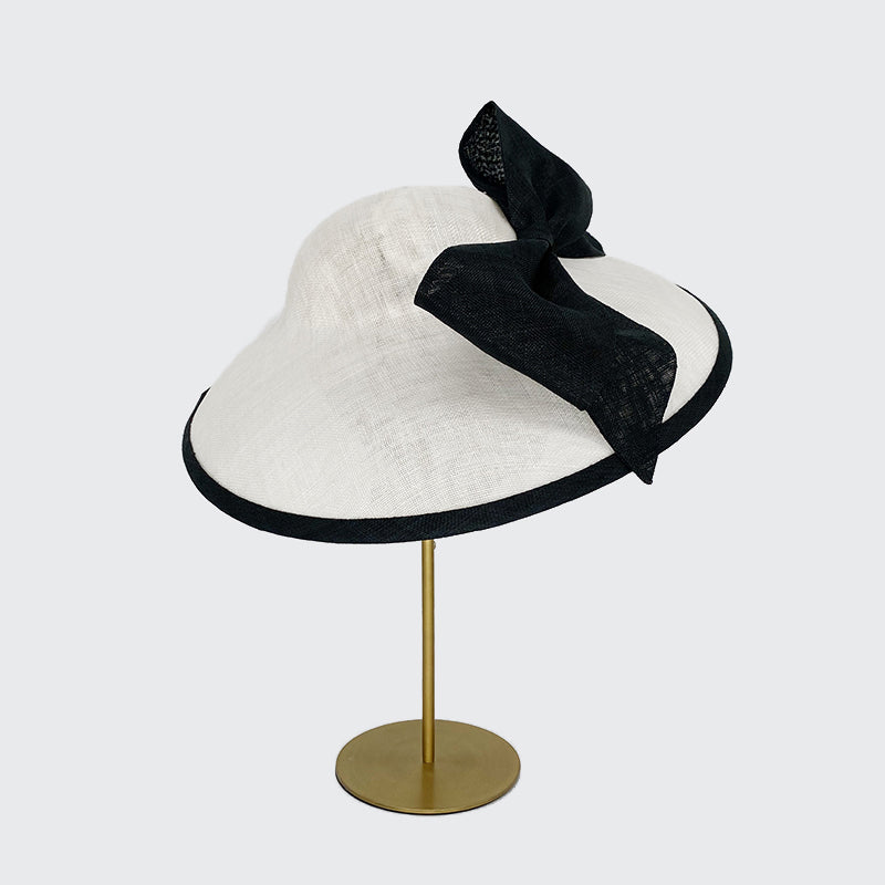 Side view of a white sweep bell with a black edge and a large bow on a linen display head