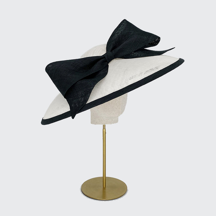 Photo of a white sweep bell with a black edge and a large bow on a linen display head