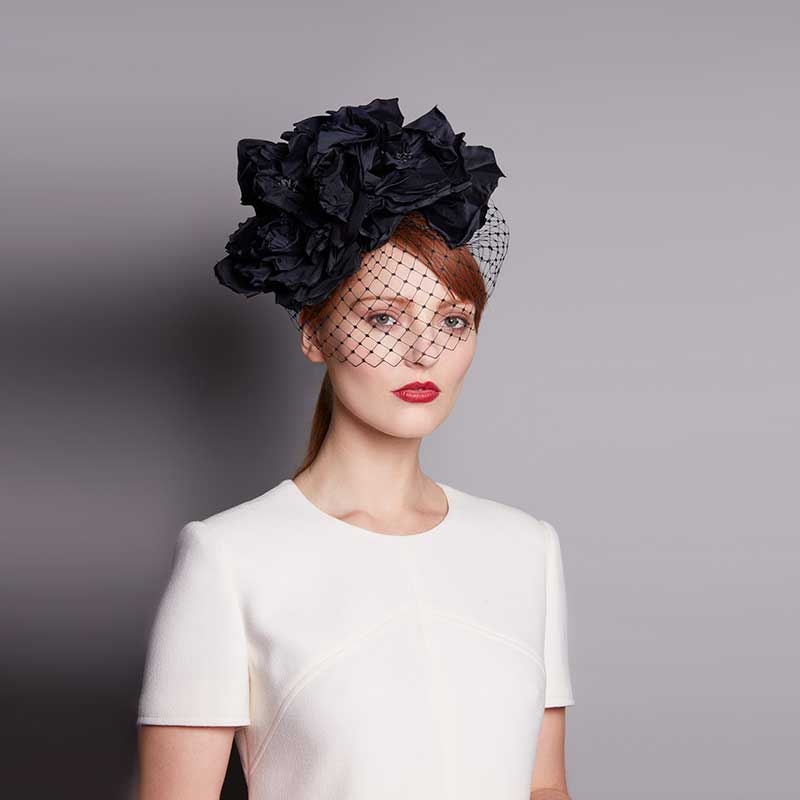 Woman with red hair wearing a white dress and a black silk flower headdress and face veil