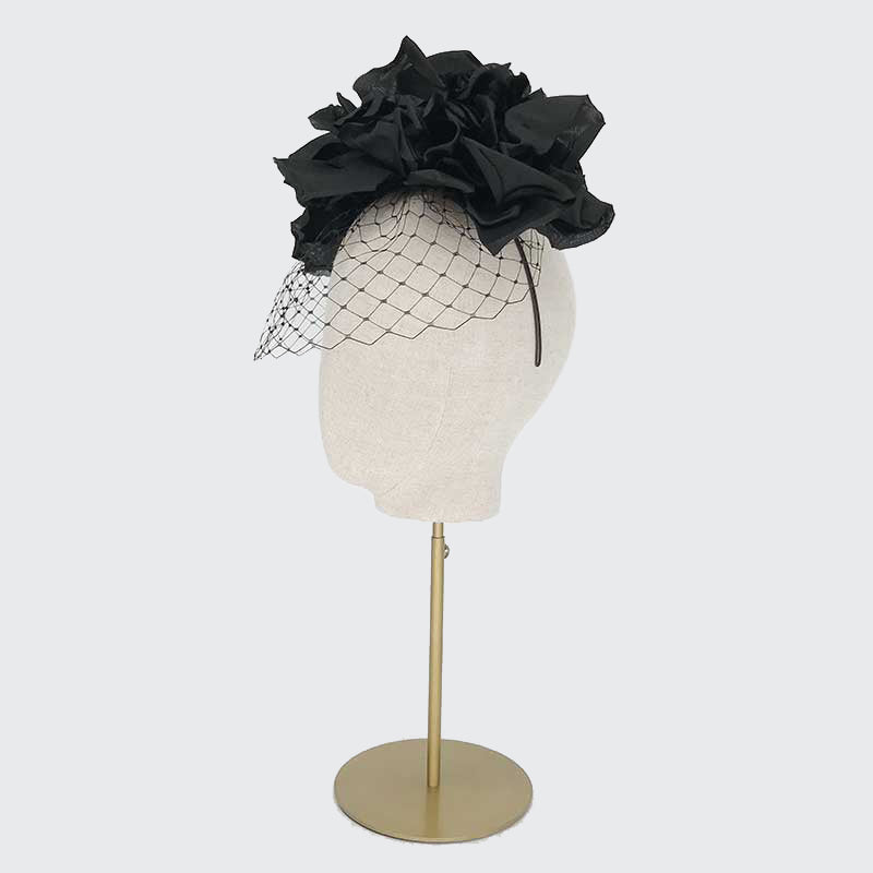 Side view of a black silk flower headdress and face veil on a linen display head