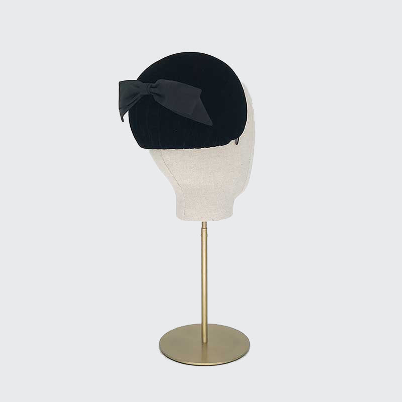 Photo of a black velvet caplet with a black bow on a linen display head