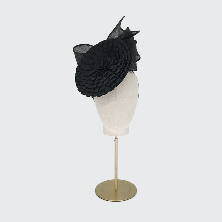 Photo of a black pleated grosgrain disc with a bow on a linen display head