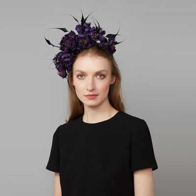 Woman with brown hair wearing a black dress and a purple silk flower headdress and black feathers