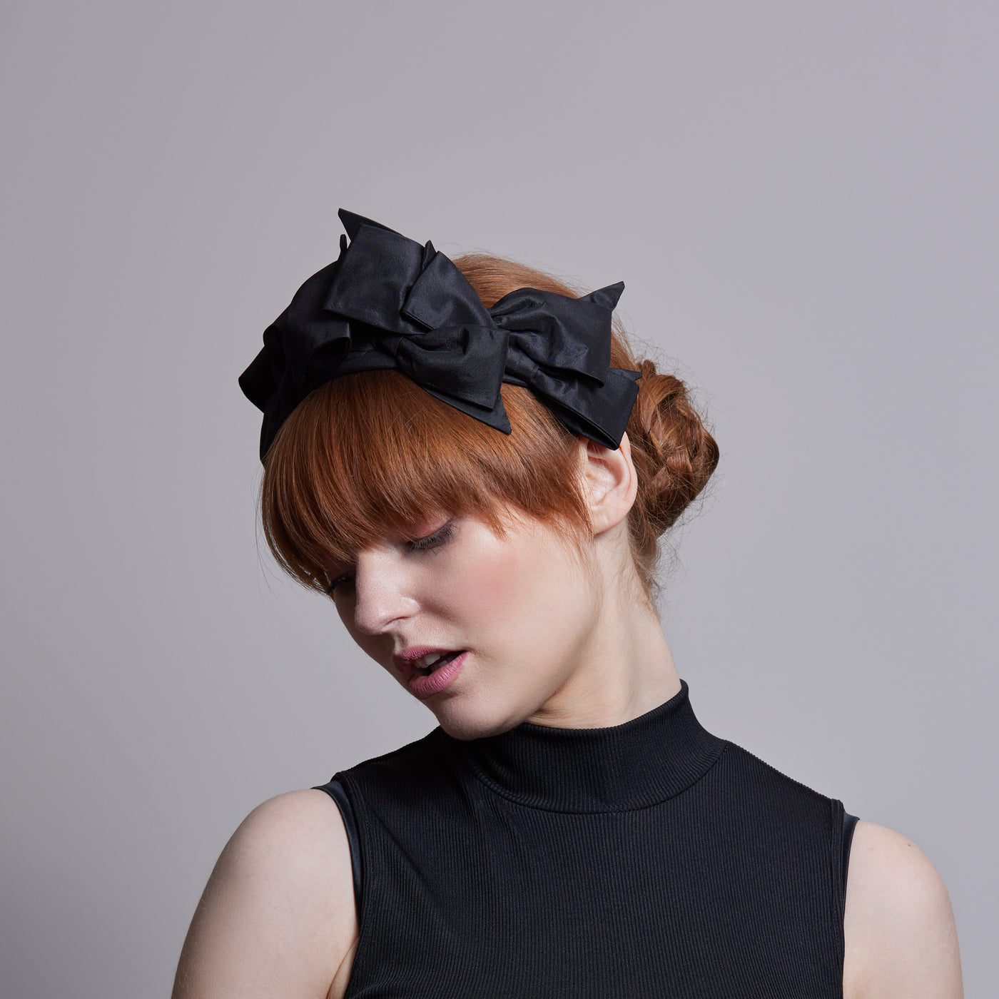 Woman with red hair wearing a black top and a black silk bow headband