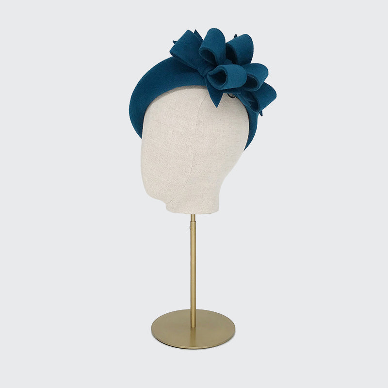 Side view of a teal velour felt beret with bows on a linen display head