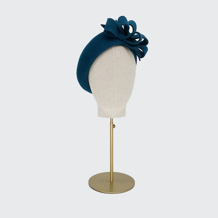 Photo of a teal velour felt beret with bows on a linen display head