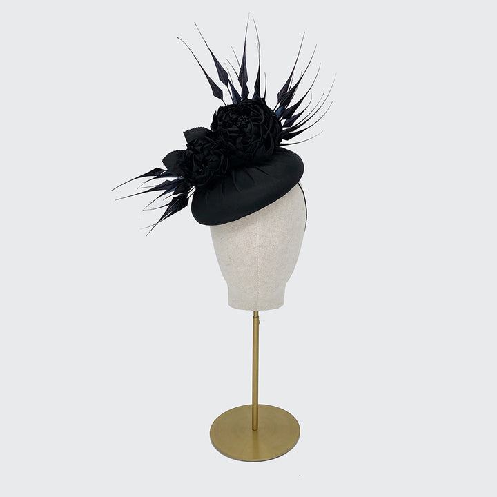 Photo of a black large silk pillbox with silk roses and diamond-cut feathers on a linen display head