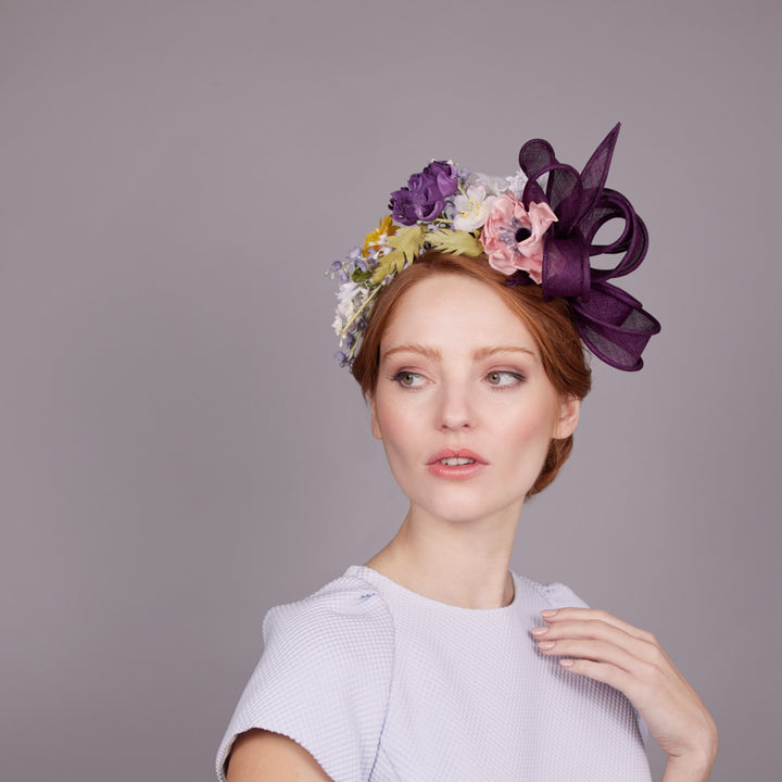 Woman with red hair wearing a pale blue dress and a purple and silk flower headband with a looped bow on the side