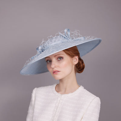 Woman with red hair wearing a white tweed jacket and a pale blue downbrim with honeycomb veiling and bows on top