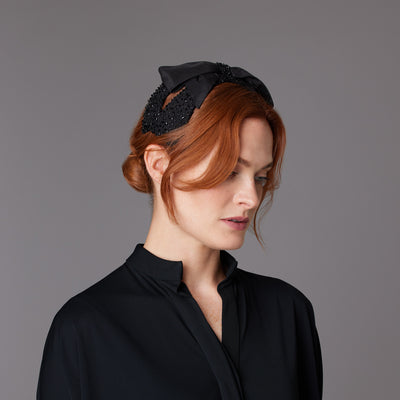 Woman with red hair wearing a black shirt and a black silk beaded bow headband