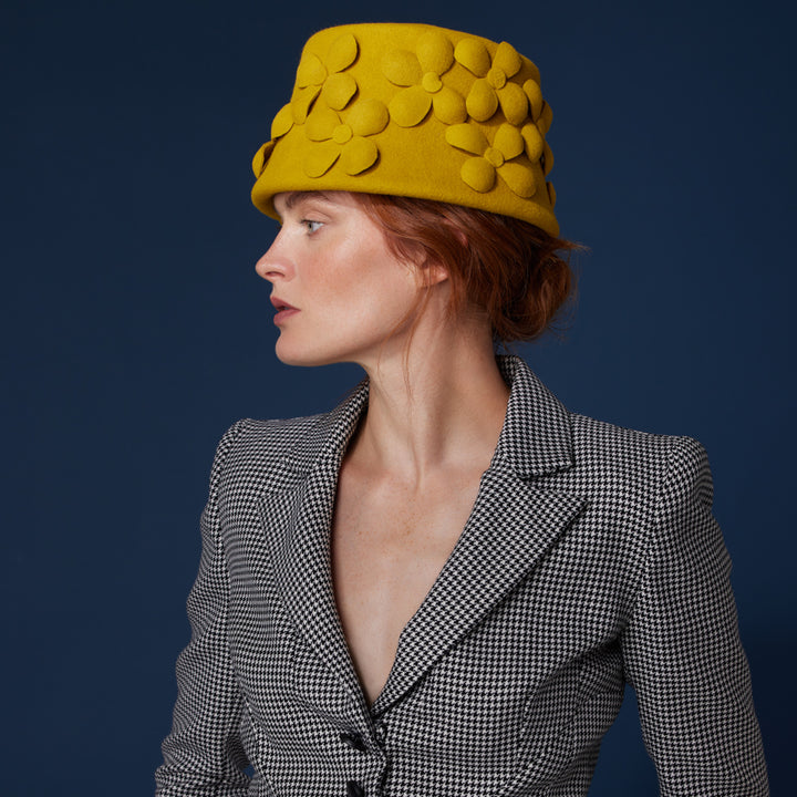 Woman with red hair wearing a houndstooth blazer and a mustard velour felt bucket with felt flowers