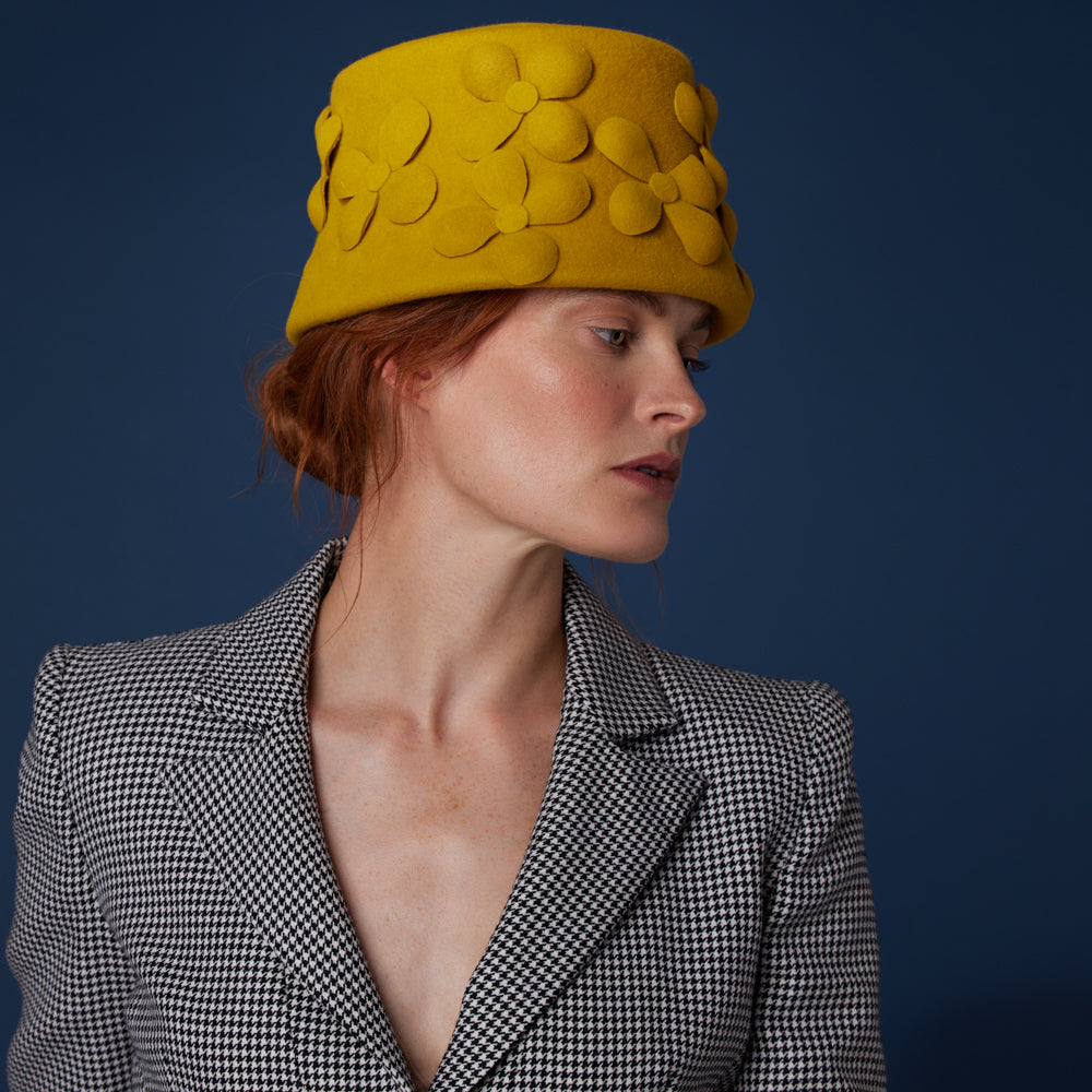 Woman with red hair wearing a houndstooth blazer and a mustard velour felt bucket with felt flowers