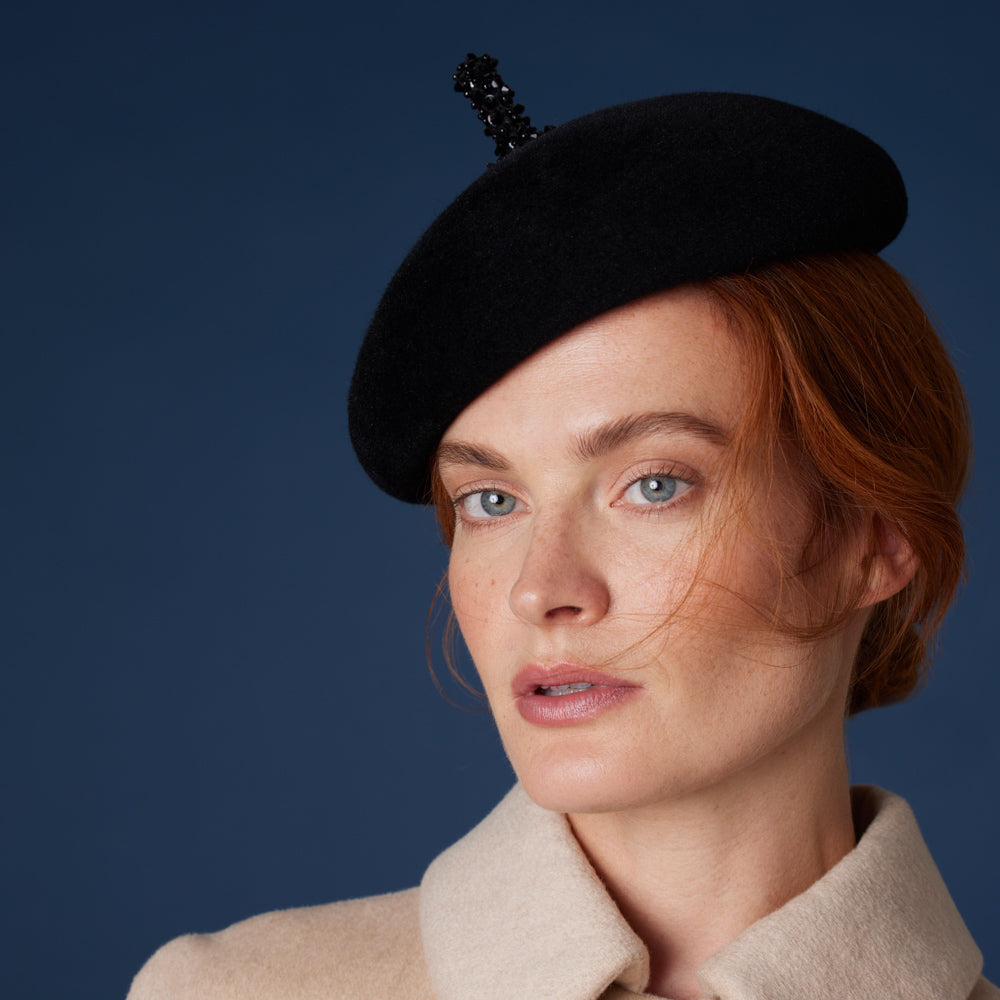 Woman with red hair wearing a cream coat and a black velour felt beret with a beaded stalk