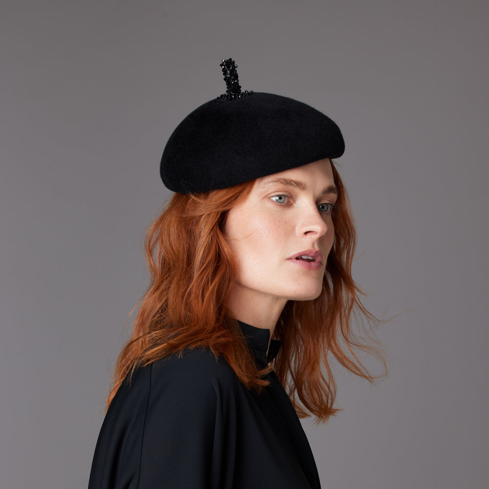 Woman with red hair wearing a black shirt and a black velour felt beret with a beaded stalk