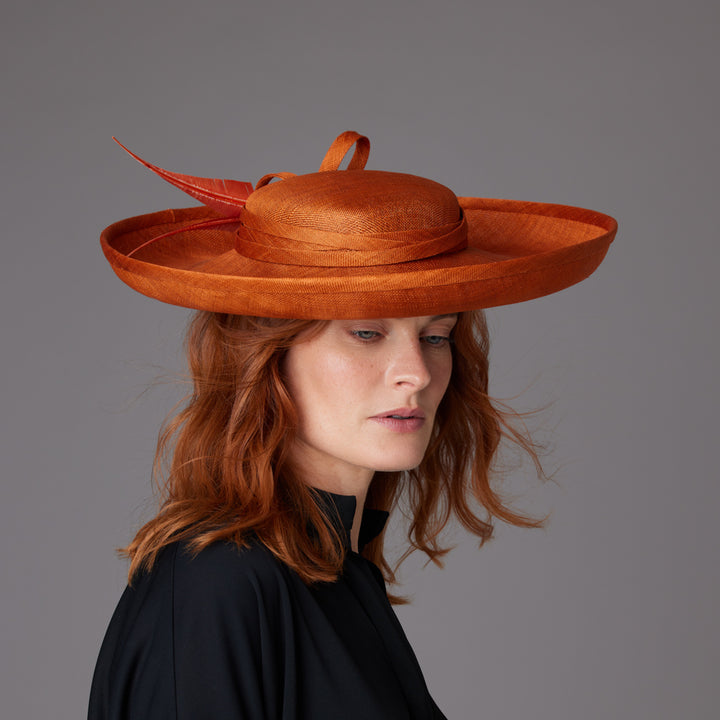 Woman with red hair wearing black shirt and a burnt orange Breton hat with sharp feathers