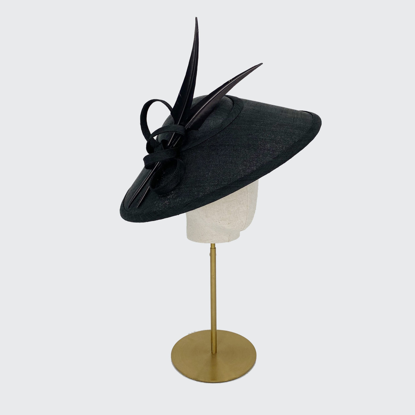 Side view of a black fine straw Charlene with black sharp feathers on a linen display head