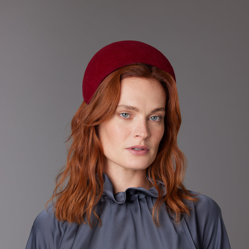Woman with red hair wearing a grey blouse and a red velour felt wide headband