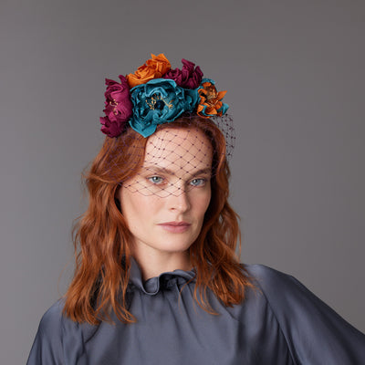 Woman with red hair wearing a grey blouse and a silk flower headband with a face veil.