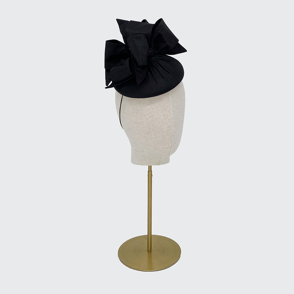 Photo of a black silk pillbox with bows on a linen display head