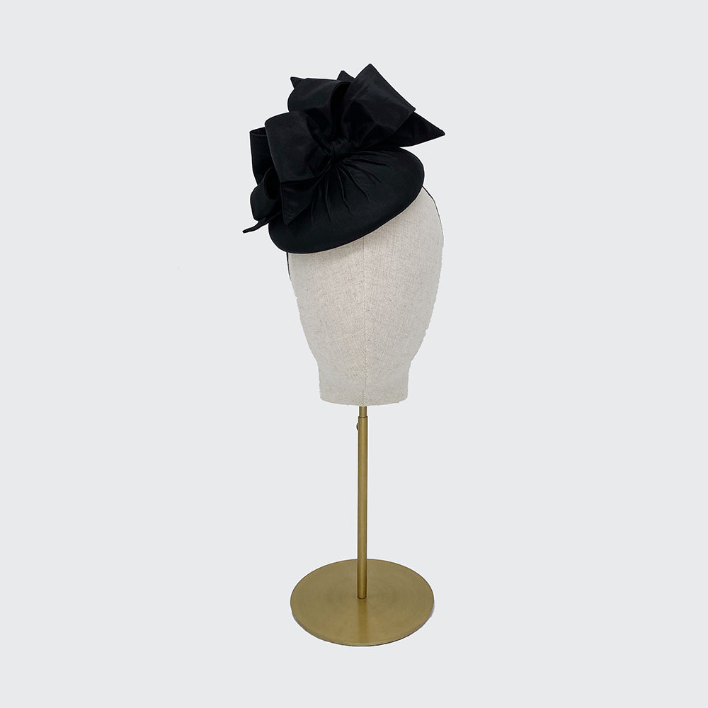Photo of a black silk pillbox with bows on a linen display head