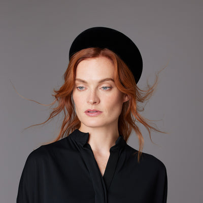 Woman with red hair wearing a black blouse and a black velvet Jackie O pillbox
