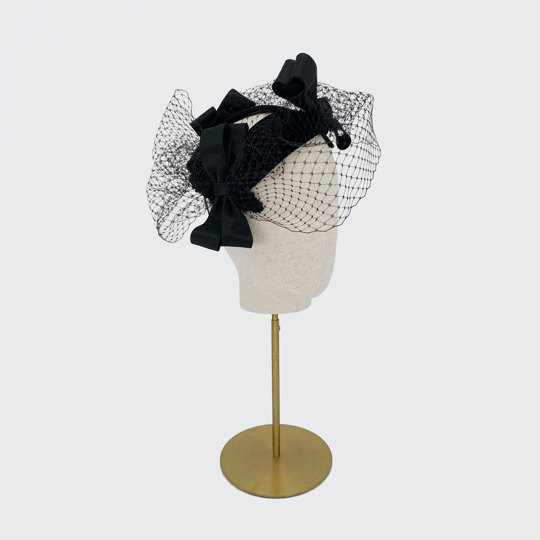Side view of a black silk trio of bows headpiece with veiling on a linen display head