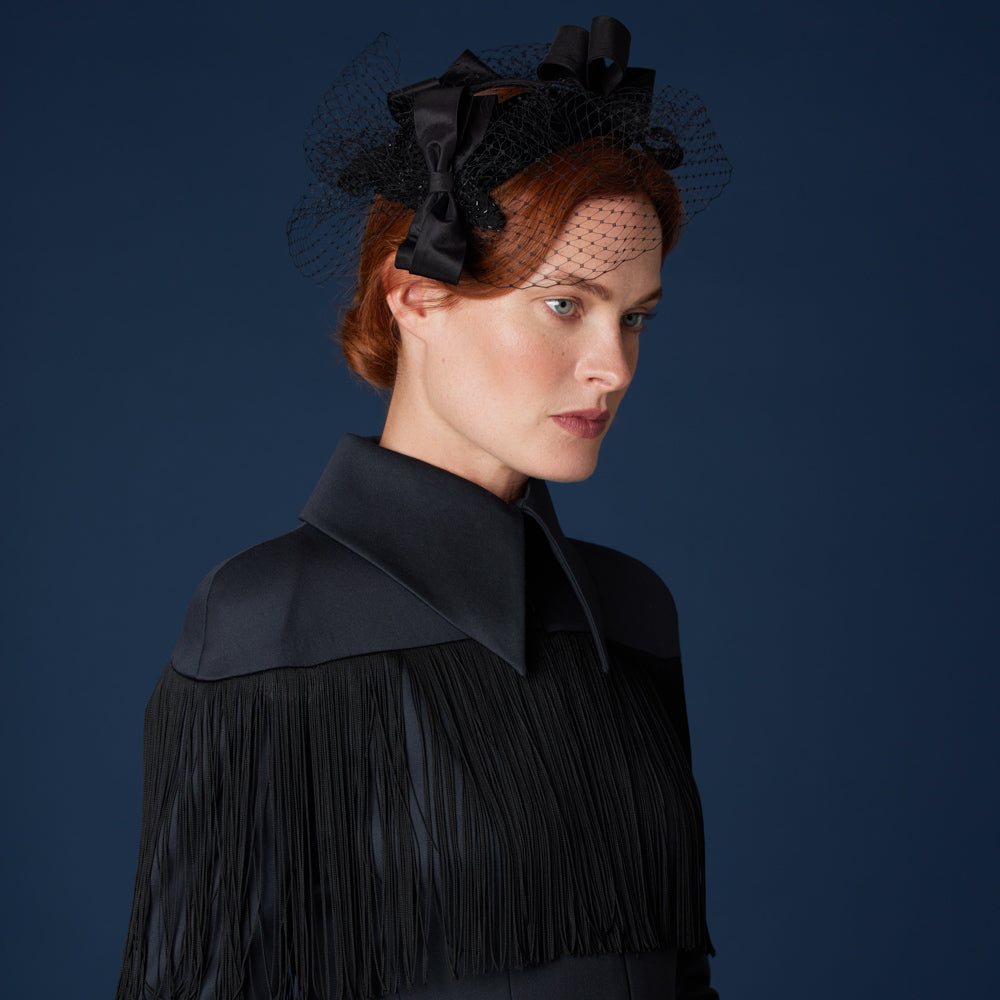 Woman with red hair wearing a black top and a silk trio of bows headpiece with veiling