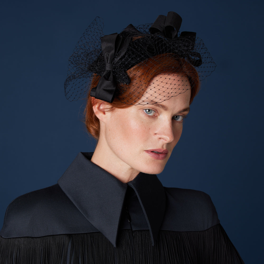 Woman with red hair wearing a black top and a silk trio of bows headpiece with veiling