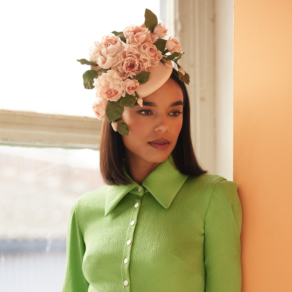 Woman with dark hair wearing a green dress and a peach silk pillbox with cascading silk roses