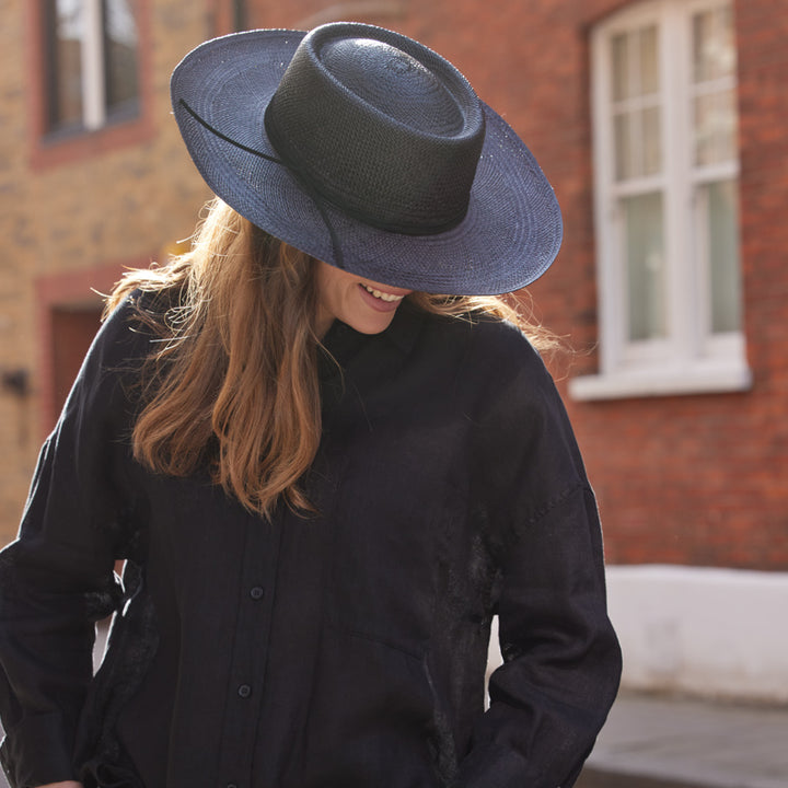 Woman with long hair wearing a balck shirt and a black panama plantation fedora with a leather band