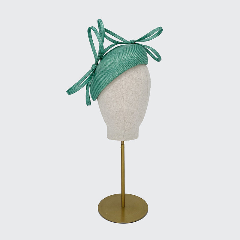 Photo of an aqua straw pillbox with bows on a linen display head