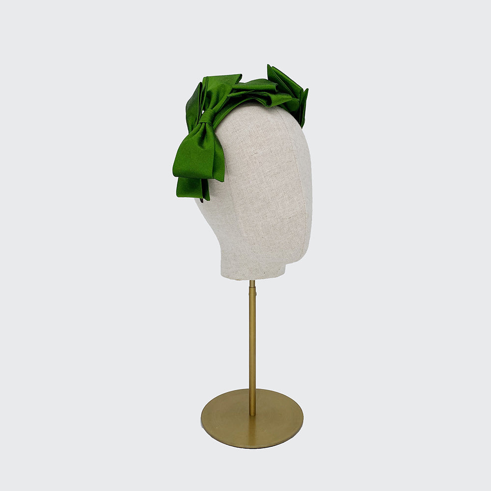 Side view of a green silk bow headband on a linen display head