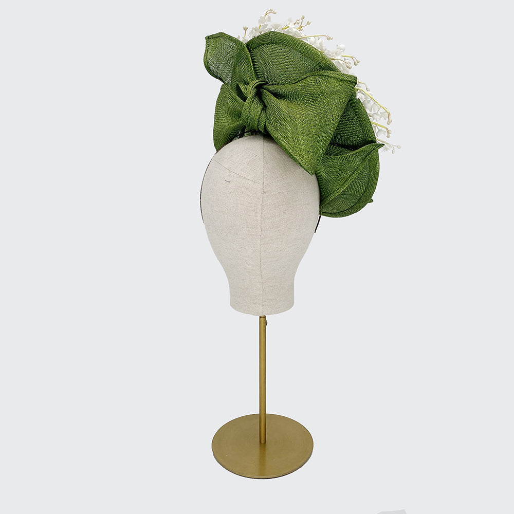 Back view of a green disc with lily of the valley around the edge and a bow on the back on a linen display head