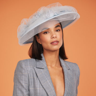 Woman with dark hair wearing a chack blazer and a pale blue straw disc with roses under gathered tulle