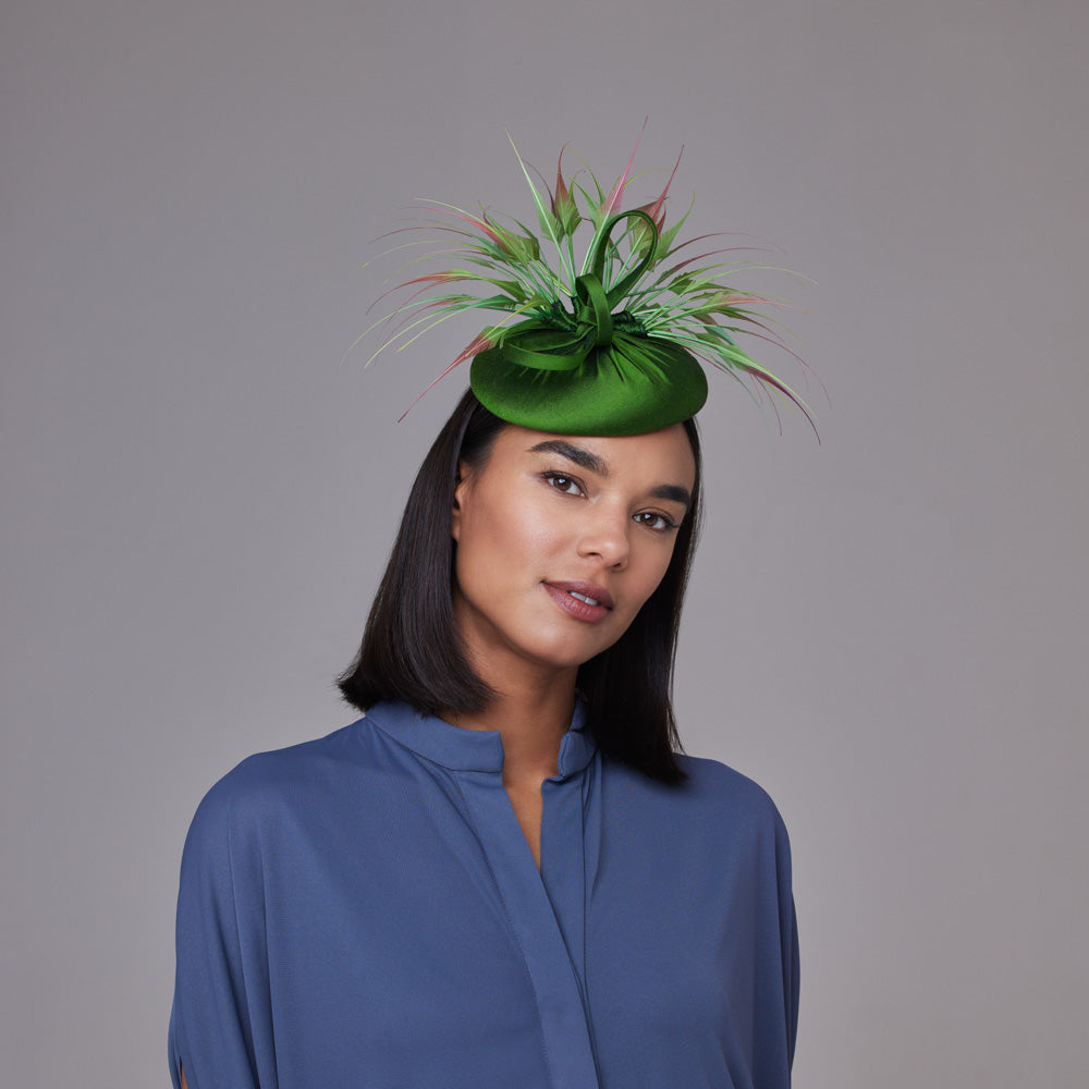 Woman with dark hair wearing a grey shirt and a leaf green silk pillbox with dip-dyed feathers