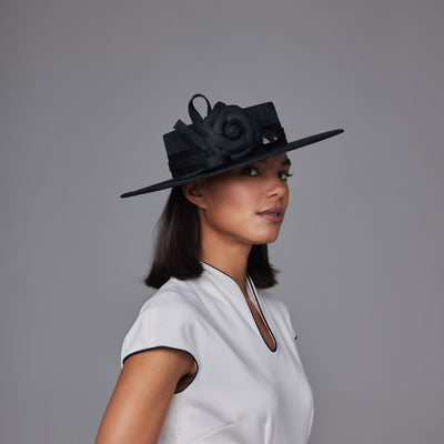 Woman with dark hair wearing a white dress and a black straw boater with a camellia and a bow
