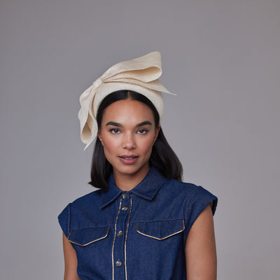 Woman with dark hair wearing a denim dress and a natural straw wide headband with a bow