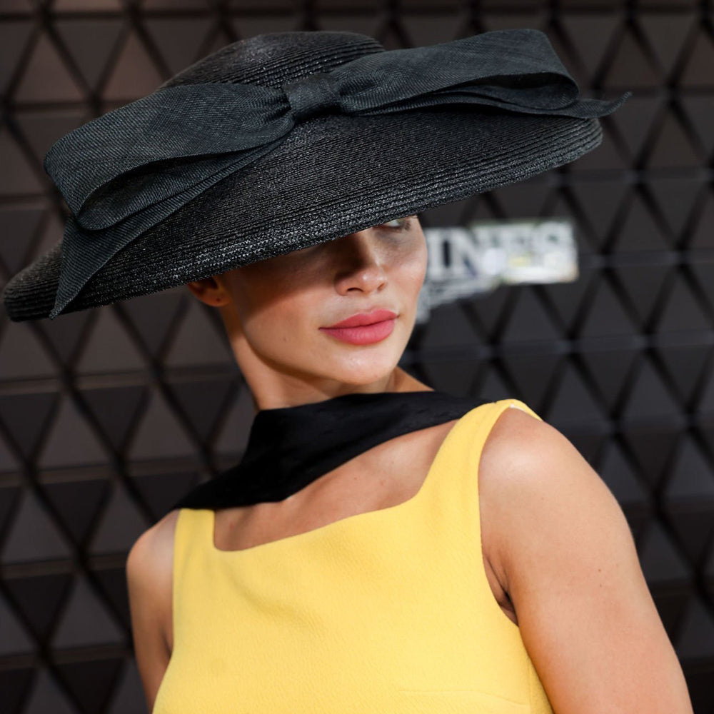 Photo of Amy Jackson wearing a yellow dress with a black scarf and a black Italian straw cut through hat with a bow