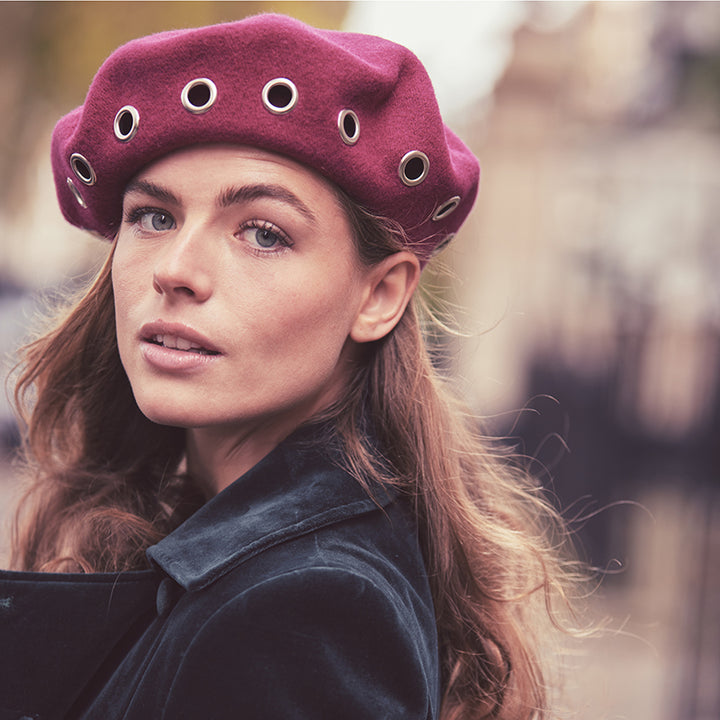Woman with long hair wearing a magenta wool beret with eyelets